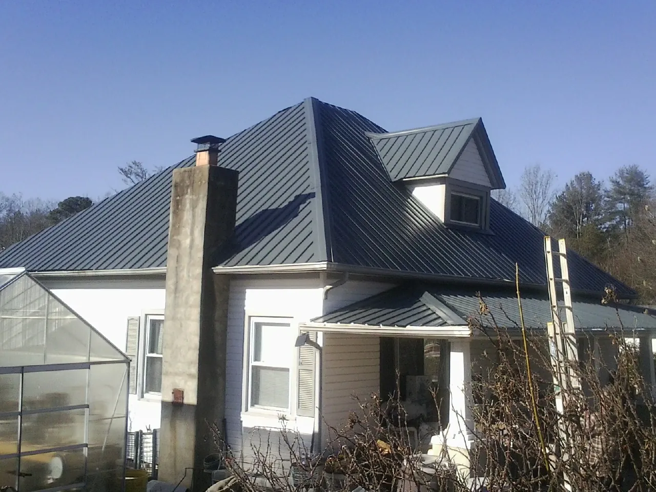 Dark blue standing seam metal roof on a white farmhouse with dormer — Slate & Tile Roof Repair by Roofing Brothers in Concho