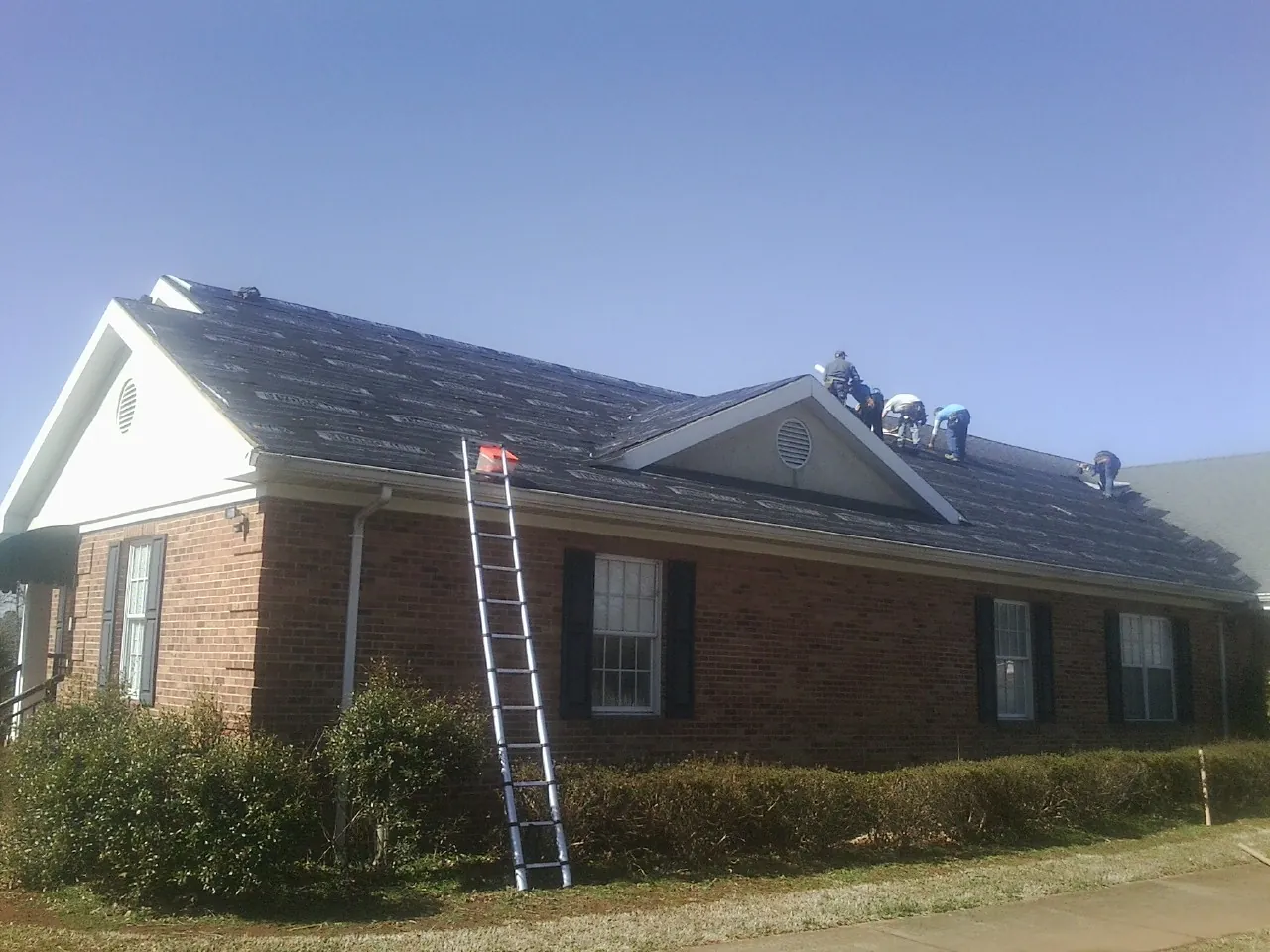 Crew tearing shingles off a brick ranch roof with a ladder set — Emergency Roof Repair work by our crew in Concho