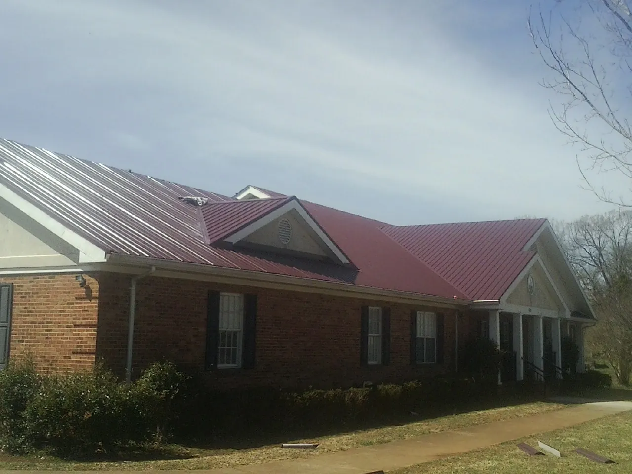 Red metal roof with gabled entries on a long brick building, from a Hail Damage Roof Repair job in Concho