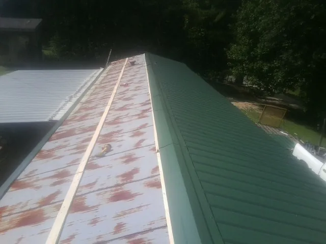 Old rusted panels beside newly installed green metal roofing — Wind Damage Roof Repair by Roofing Brothers in Concho