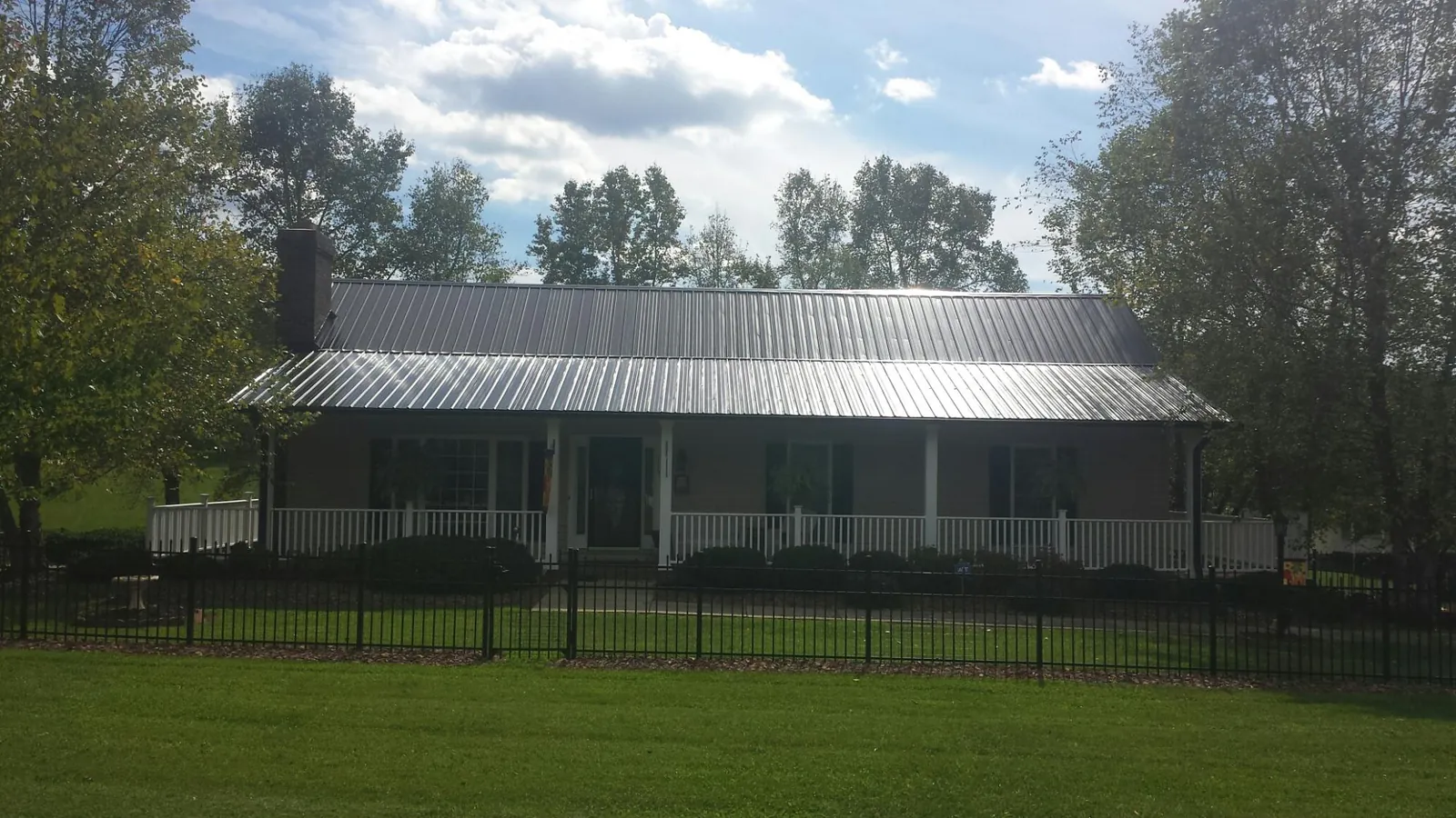 Gray metal roof on a brick ranch with a full width front porch — Gutter Guard Installation work by our crew in Concho