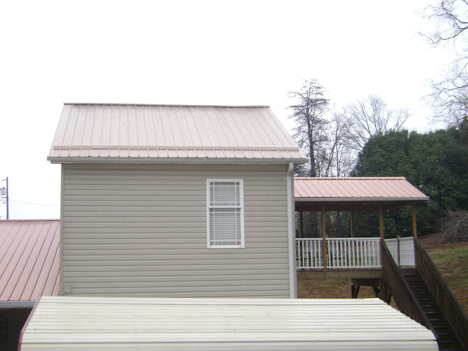 Tan metal roofs on a two story addition and attached porch, from a Roof Replacement job in Concho